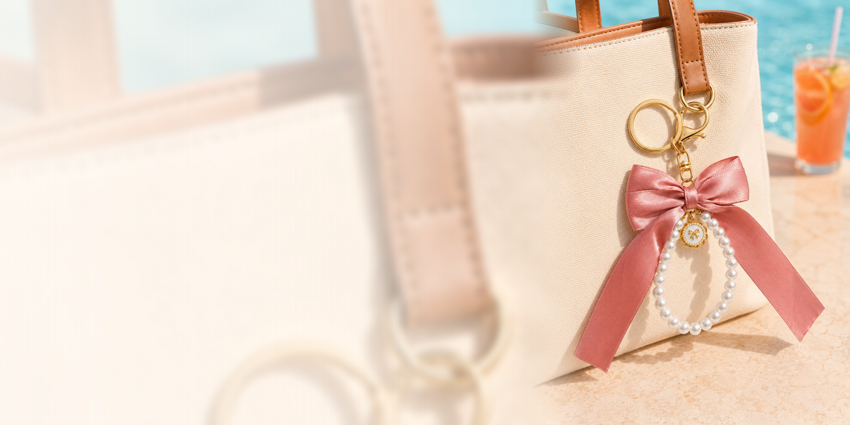 Pink bow pearl bag charm clipped to a cream tote by the pool
